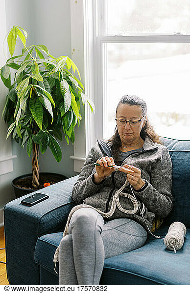 Middle Aged woman sitting on a blue sofa while crocheting to unwind