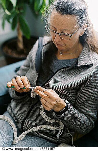 Middle Aged woman sitting on a blue sofa while crocheting to unwind
