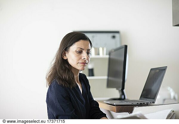 Middle-aged woman with dark hair controls product at work with laptop and folder  Freiburg  Baden-Württemberg  Germany  Europe