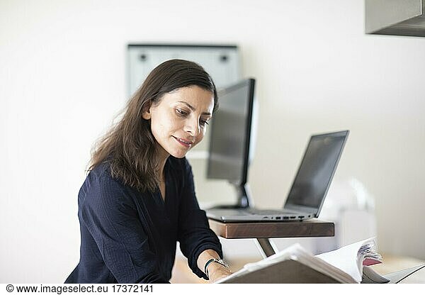 Middle-aged woman with dark hair controls product at work with laptop and folder  Freiburg  Baden-Württemberg  Germany  Europe