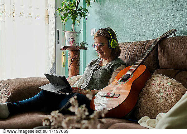Middle-aged woman with headphones learn to play the guitar at home