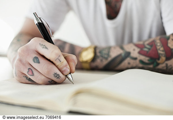 Midsection of a tattooed man writing