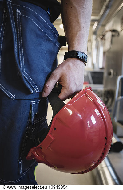 Midsection of auto mechanic teacher holding red hardhat at workshop