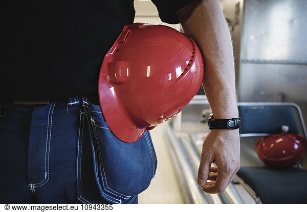 Midsection of auto mechanic teacher with red hardhat while standing at workshop