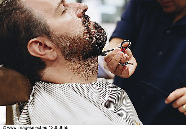 Midsection of barber cutting man beard at salon