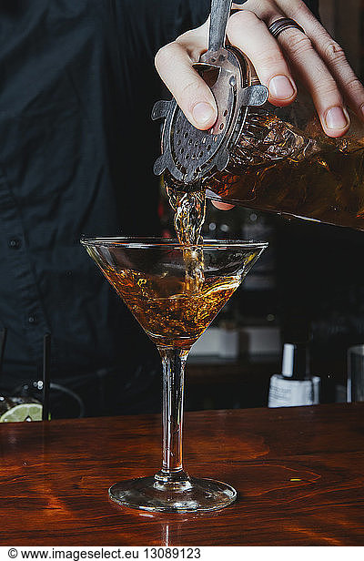 Midsection of bartender pouring alcohol in martini glass on table