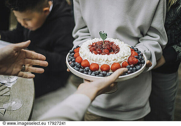 Midsection of boy giving fresh cake to woman at birthday