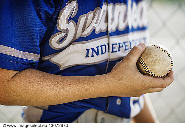 Midsection of boy holding baseball in dugout