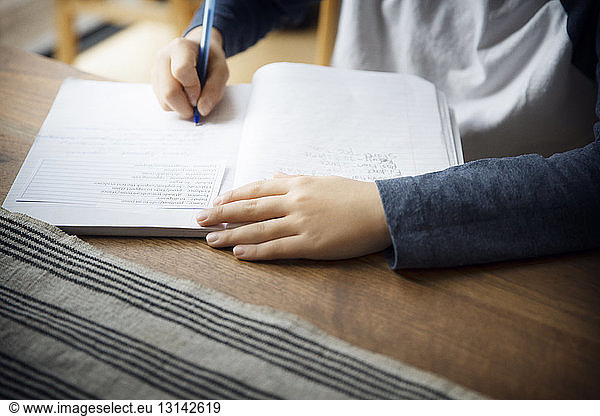 Midsection of boy writing in book on table at home
