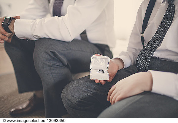 Midsection of bridegroom sitting by pageboy holding wedding ring while sitting on bed at home