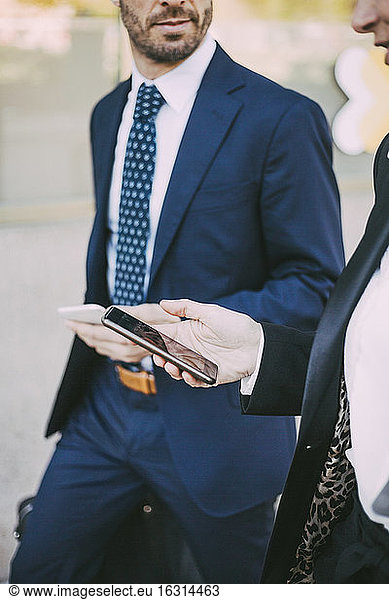 Midsection of business colleagues with smart phone in city