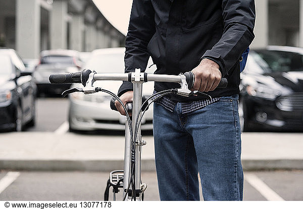 Midsection of businessman holding bicycle on city street