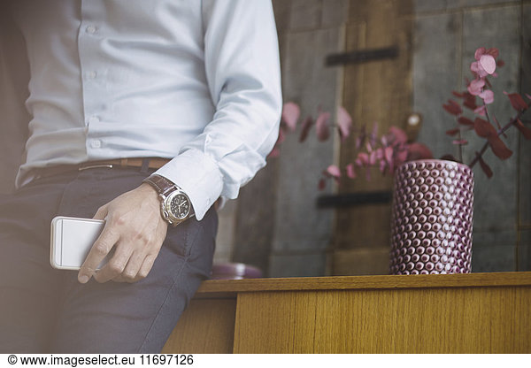 Midsection of businessman holding mobile phone while leaning on sideboard in portable office truck