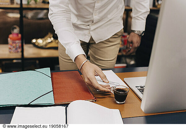 Midsection of businessman picking up coffee cup from desk in office