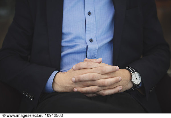 Midsection of businessman sitting with hands clasped at airport