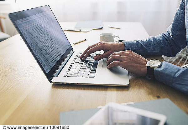 Midsection of businessman using laptop computer at desk in office
