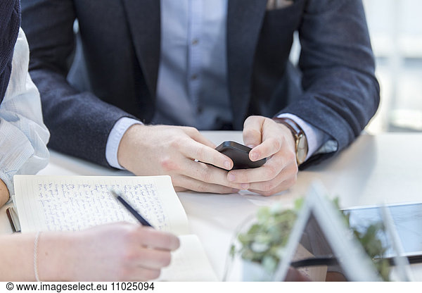 Midsection of businessman using phone while sitting with female colleague in meeting