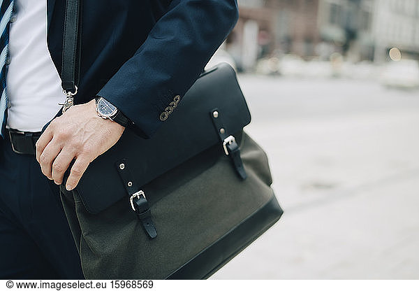 Midsection of businessman with bag standing in city