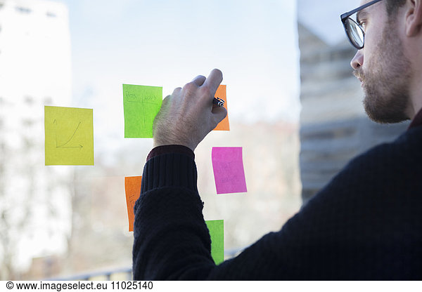 Midsection of businessman writing on adhesive note in office