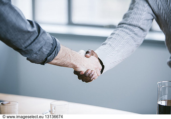 Midsection of businessmen handshaking in board room
