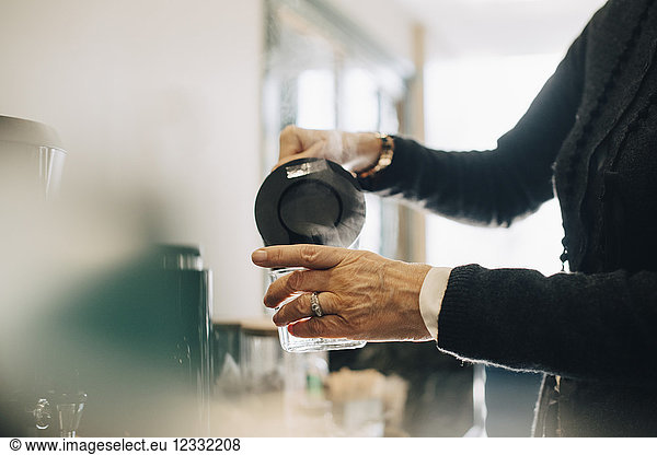 Midsection of businesswoman pouring hot water in drinking glass while standing at office