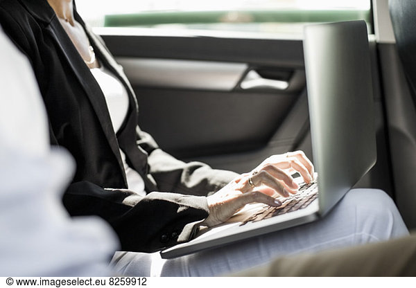 Midsection of businesswoman using laptop in taxi