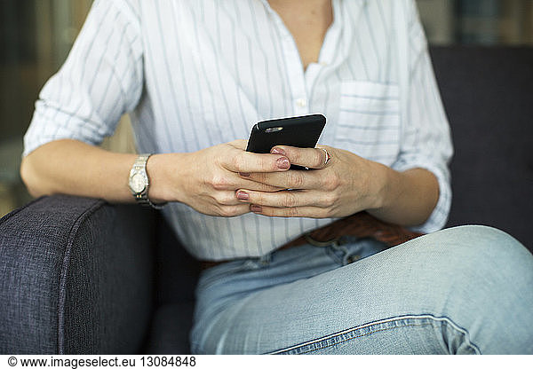 Midsection of businesswoman using mobile phone while sitting on sofa at office