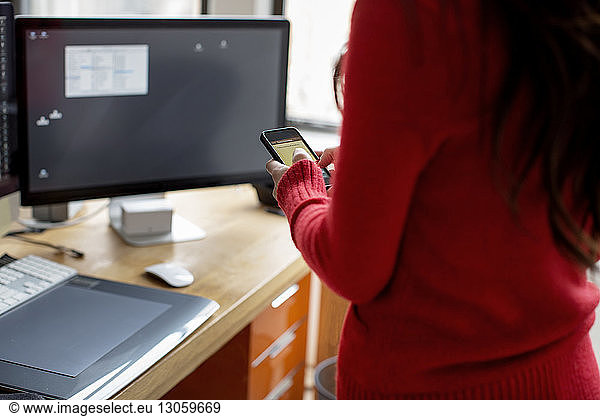 Midsection of businesswoman using phone at computer desk