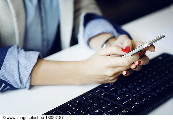 Midsection of businesswoman using phone by keyboard at desk