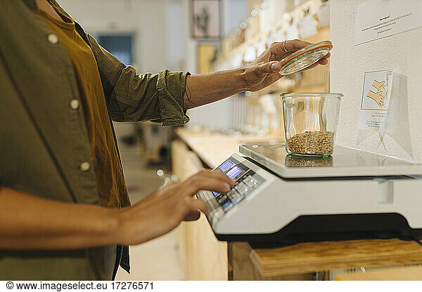 Midsection of businesswoman weighing grain jar on weight scale in cafe