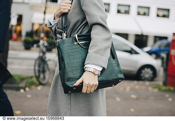 Midsection of businesswoman with handbag standing in city