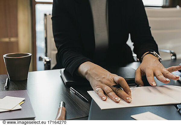 Midsection of businesswoman with pen and diary at desk in office