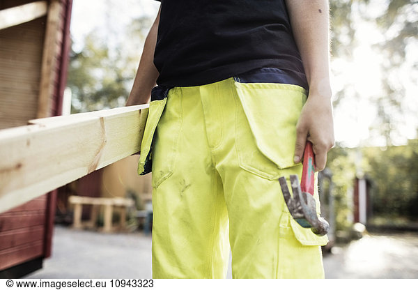 Midsection of carpentry student holding hammer and wooden planks