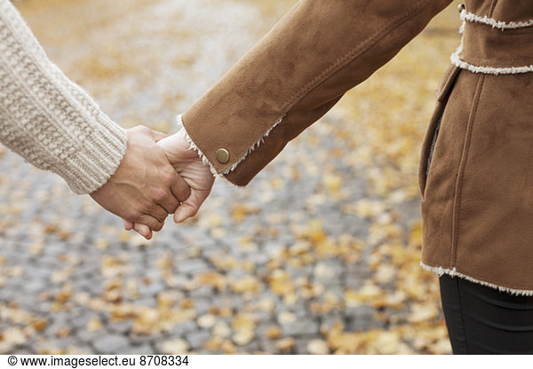 Midsection of couple holding hands during autumn