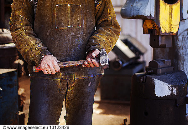 Midsection of craftsperson holding hammer at metal industry