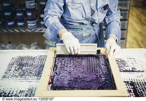 Midsection of craftswoman using silk screen to print design on fabric at workshop