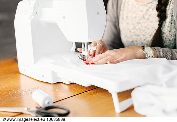 Midsection of design professional using sewing machine at table in studio