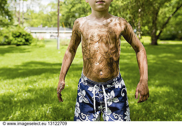 Midsection of dirty shirtless boy standing on grassy field in backyard