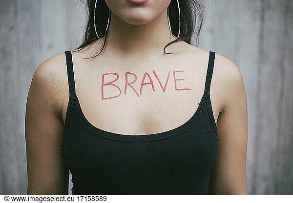 Midsection of female activist with brave text written on chest against wall