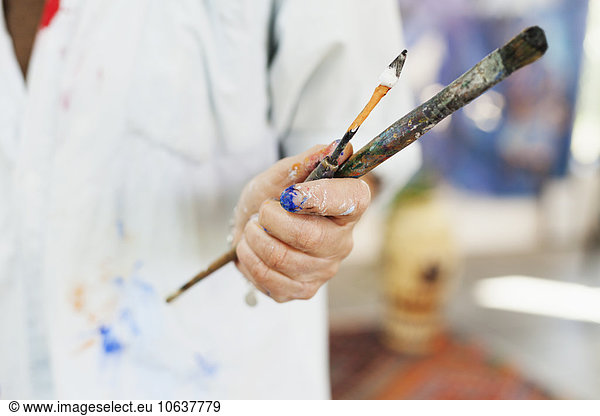 Midsection of female artist holding paintbrushes at art studio