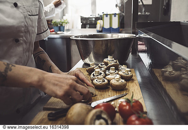 Midsection of female chef cutting mushrooms at kitchen counter
