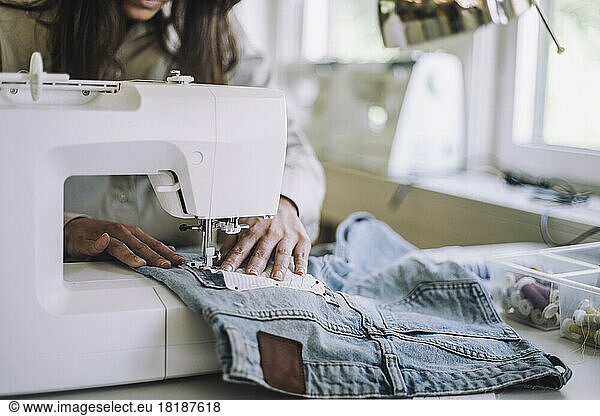 Midsection of female design professional stitching fabric through sewing machine at workshop
