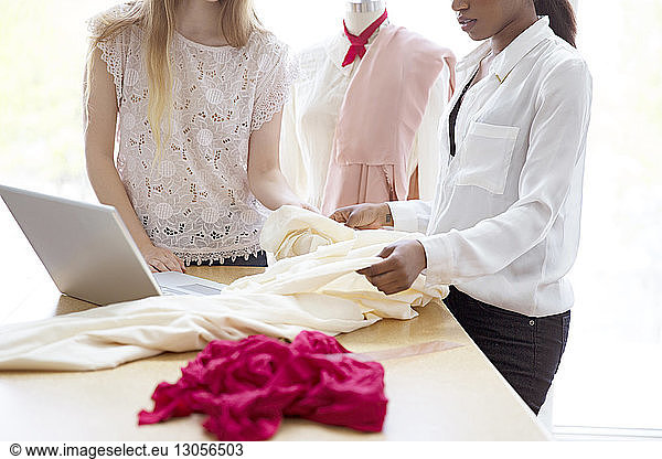 Midsection of female designers checking fabric by laptop at desk