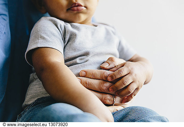Midsection of female doctor holding baby boy against white background