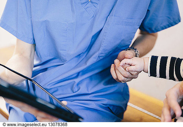 Midsection of female doctor holding baby boy's hand at hospital