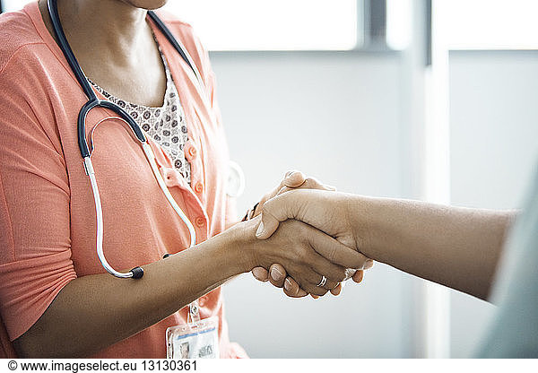 Midsection of female doctor shaking hands with patient