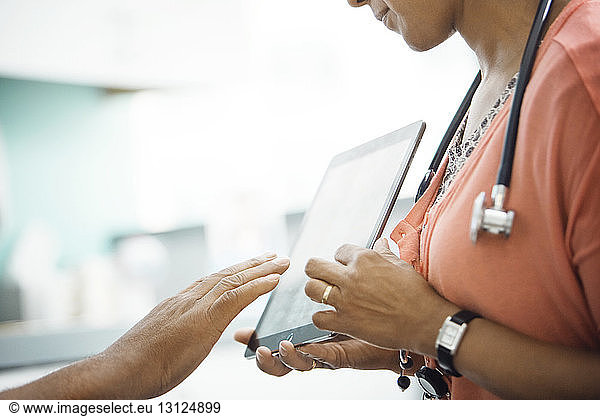 Midsection of female doctor showing report on tablet computer to patient in clinic