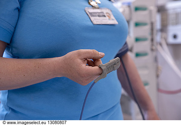 Midsection of female doctor using pulse oximeter in hospital