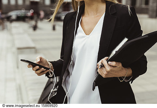 Midsection of female entrepreneur with mobile phone standing on sidewalk