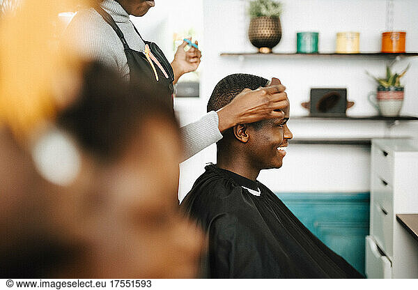 Midsection of female hairdresser cutting hair of smiling male customer in barber shop